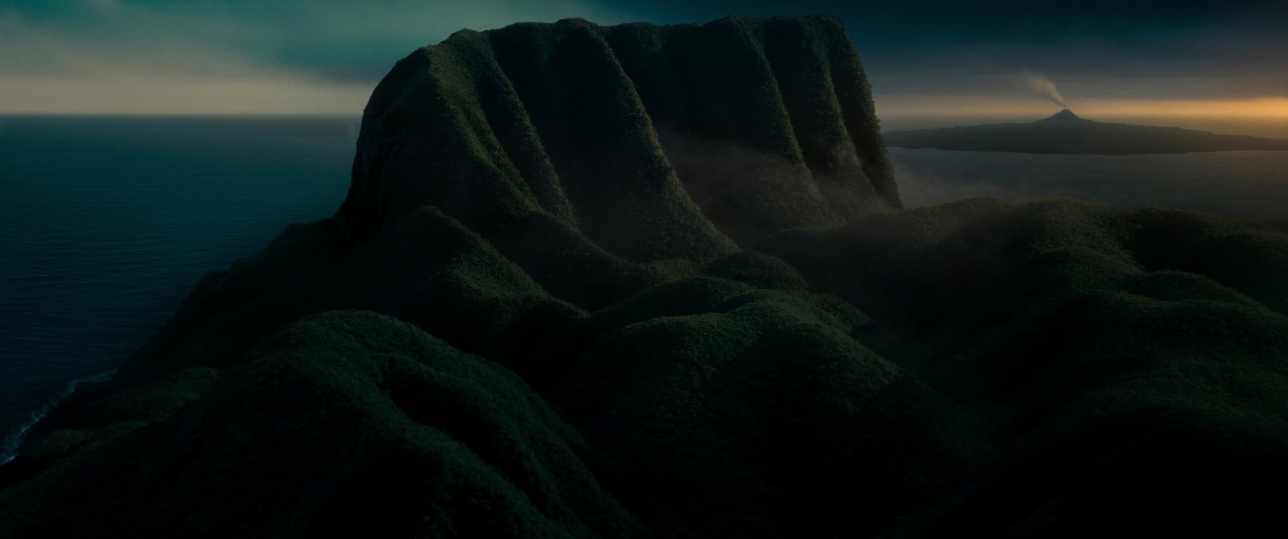 Vista aérea de una isla volcánica al amanecer, con selva densa y un volcán humeando al fondo