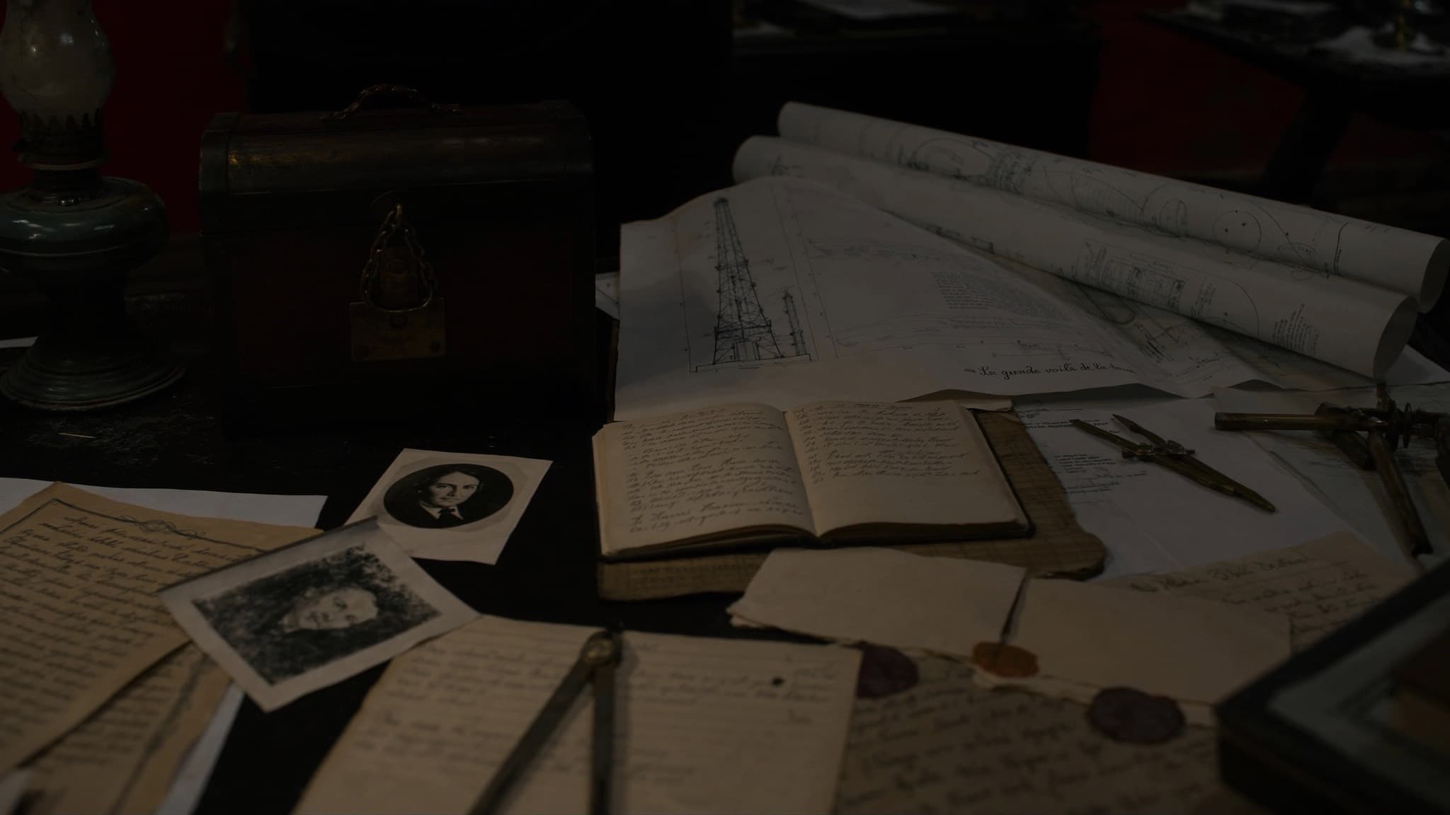 Escritorio antiguo con planos, fotografías, instrumentos de dibujo y una caja cerrada con candado