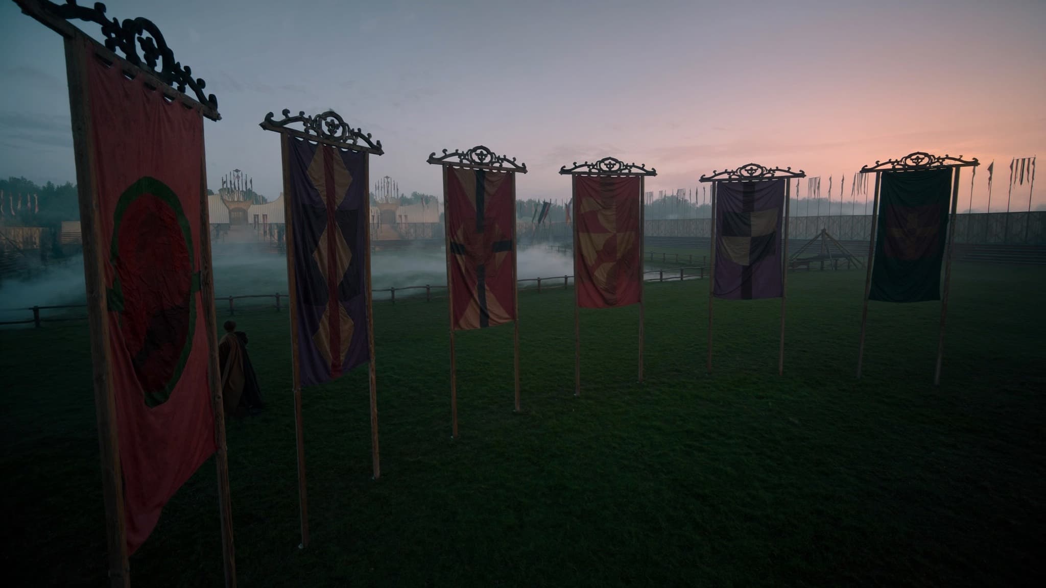 Seis estandartes medievales ondeando en un campo de torneo con niebla al amanecer