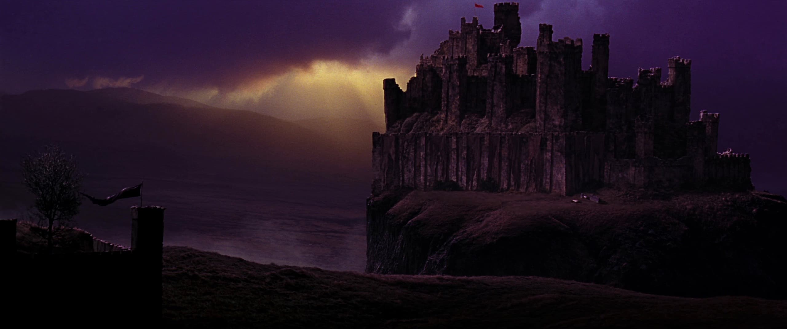 Fortaleza medieval de piedra sobre un risco al atardecer tormentoso, con estandartes al viento