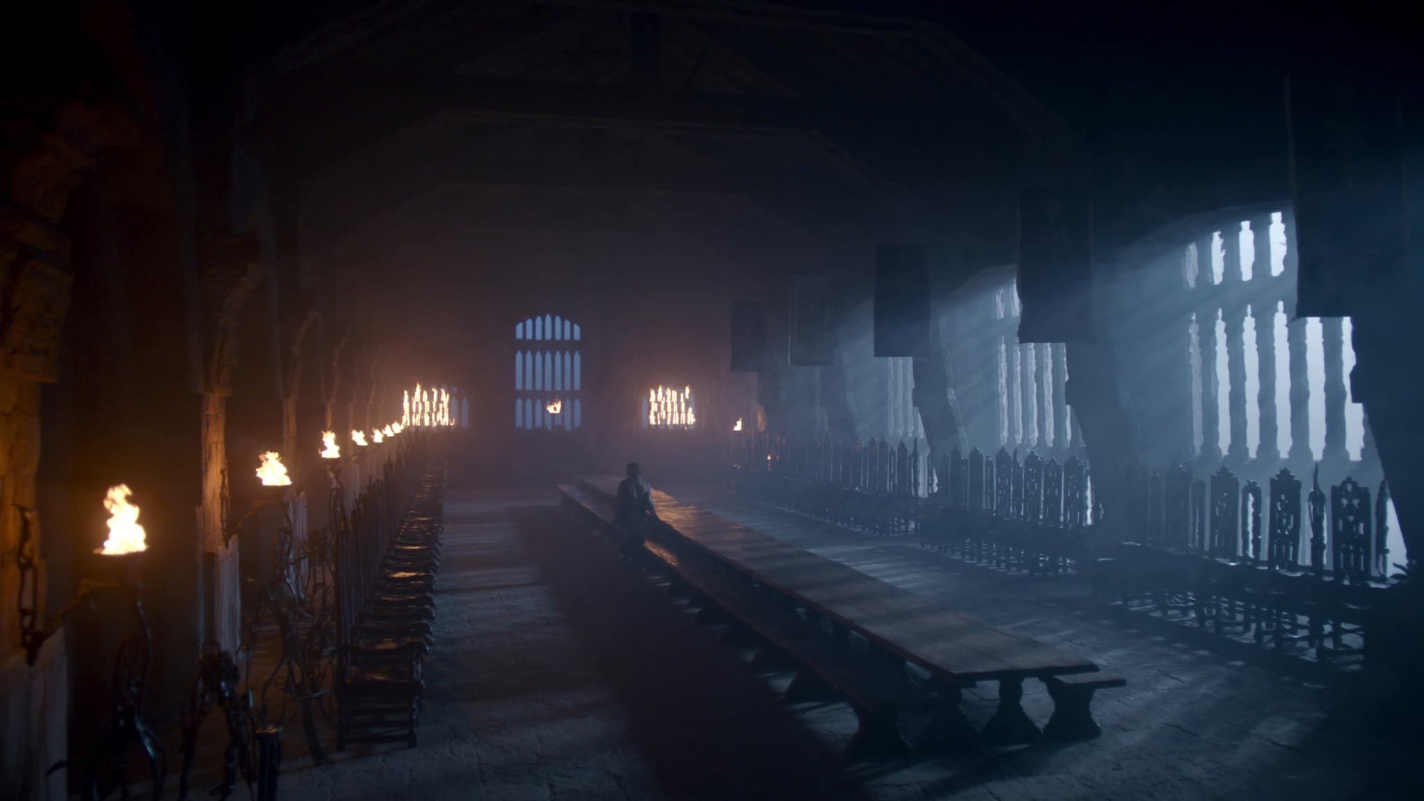 Interior de un gran salón medieval de piedra iluminado por antorchas